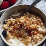 Bowl of creamy scrambled oats topped with fresh fruits and nuts