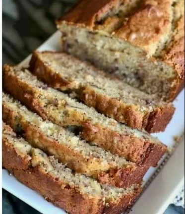 Sliced moist banana bread with sour cream on a wooden cutting board.