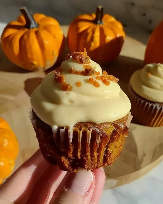 Pumpkin Cupcakes with Brown Sugar Frosting 2 Pumpkin cupcakes topped with brown sugar frosting on a rustic wooden table.