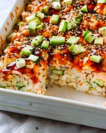 Baked sushi dish with layers of rice, seafood, and toppings in a casserole dish